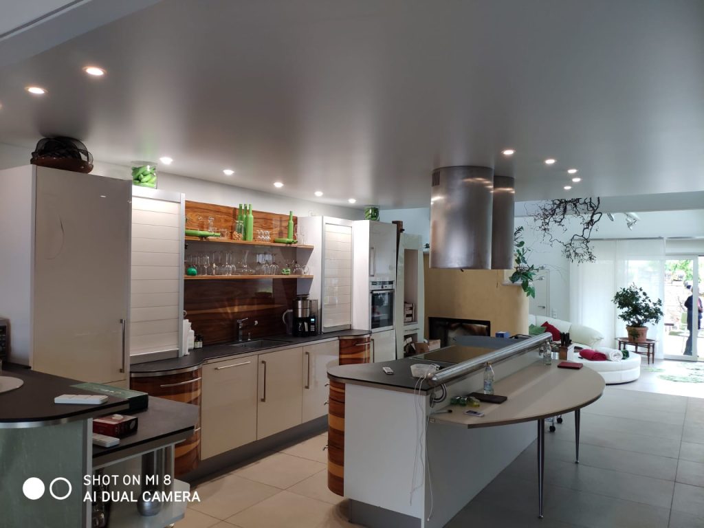 Moderne Küche mit satinierter Spanndecke, integrierten LED-Spots und offenem Wohnbereich