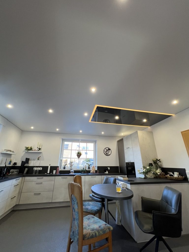 Moderne Küche mit Spanndecke, integrierten LED-Spots und beleuchtetem Deckenfeld über der Kochinsel